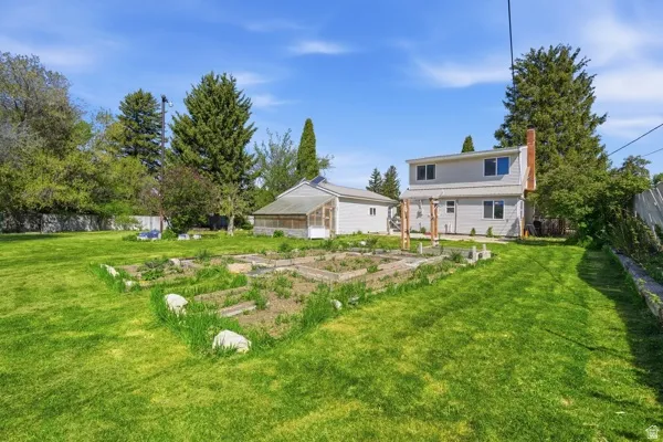 Expansive backyard featuring a manicured lawn, established garden beds, and mature trees