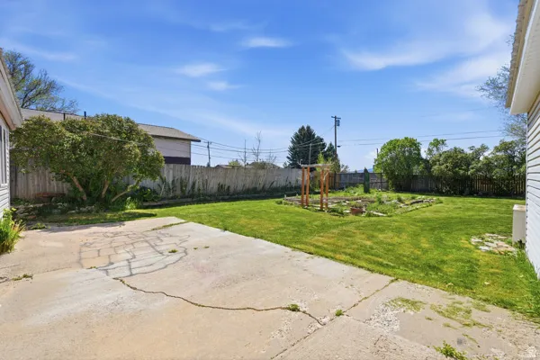 Expansive backyard featuring a concrete patio, mature trees, a wooden privacy fence, and a raised garden bed