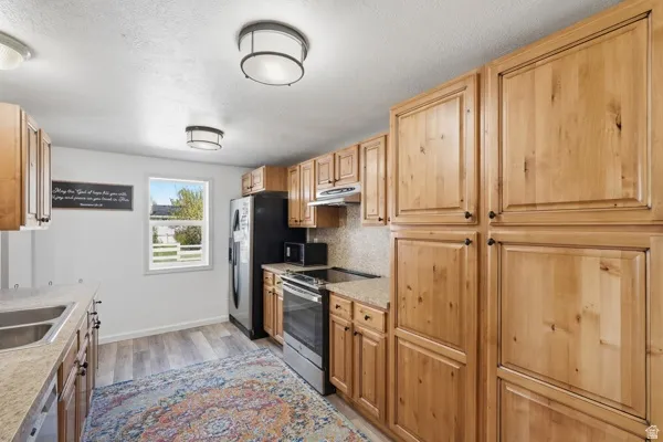 Well-appointed kitchen featuring extensive wood cabinetry, wood-finish flooring, a stainless steel electric range, and a dual basin sink