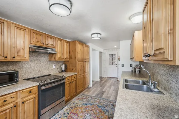 Kitchen featuring wood cabinetry, stainless steel sink, built-in range, stone-finish countertops, and wood-finish flooring