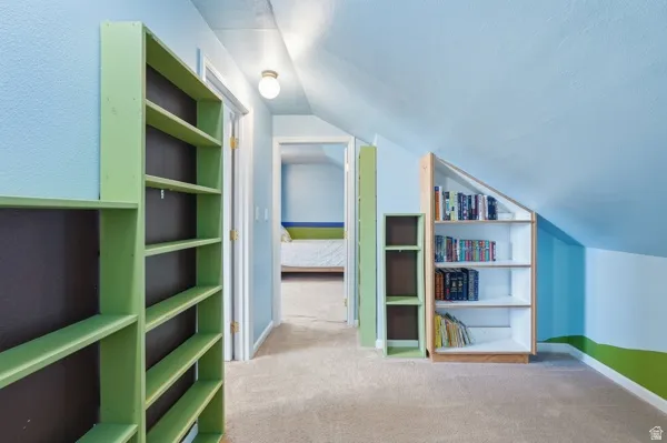 Carpeted attic space featuring built-in shelving, sloped ceilings, and a flush mount light fixture