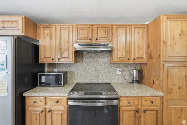 Kitchen featuring extensive light wood cabinetry, stone-finish countertops, and a full-height stone-finish backsplash