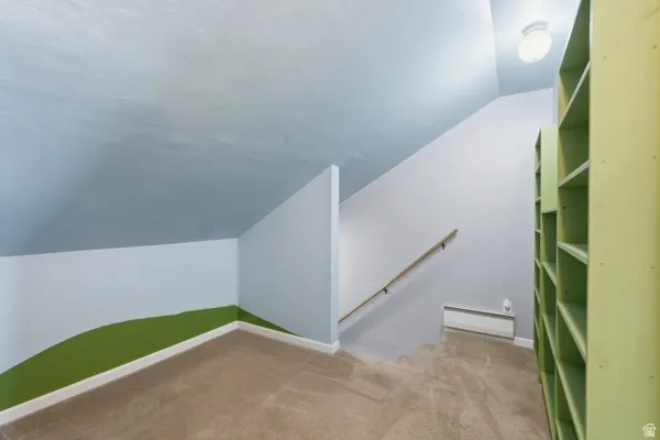 Carpeted attic space with built-in shelving, sloped ceilings, and a wall-mounted handrail