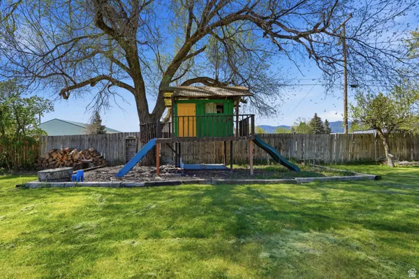 Expansive backyard featuring a mature tree, a privacy fence, and a built-in play structure with two slides