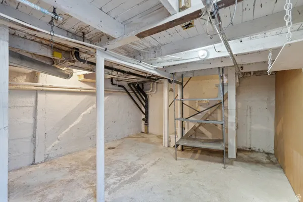 Unfinished basement space featuring exposed ceiling joists, concrete flooring, and a utility staircase