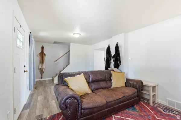 Living area featuring wood-finish flooring, white walls, and a staircase with a wooden handrail