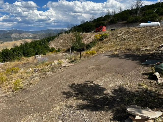 Expansive mountain property featuring a graded dirt lot, mature trees, and distant mountain ranges