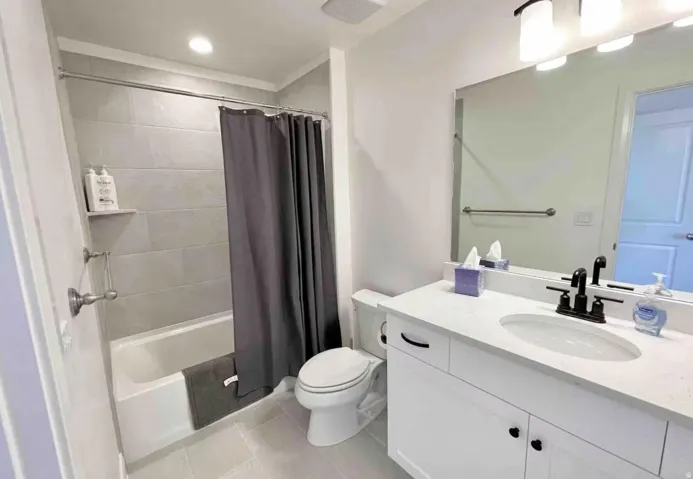Full bathroom featuring a tub/shower combination with light gray tile surround, a white vanity with a white countertop, and a large wall mirror