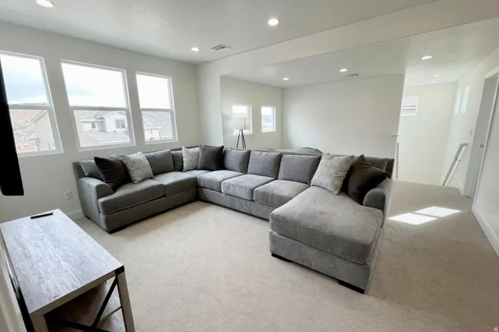 Carpeted loft area featuring multiple windows, recessed lighting, and white walls