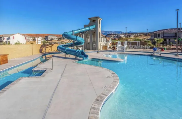 Community pool area featuring a winding water slide, a separate shallow water feature, ample concrete decking, and distant mountain scenery