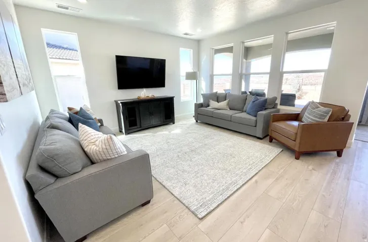 Spacious living area featuring light wood-finish flooring, a contemporary entertainment console, recessed lighting, and a series of tall windows