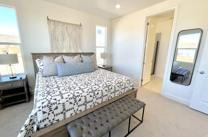 Bright bedroom featuring white walls, light-toned carpet, recessed lighting, and a doorway opening to an additional room