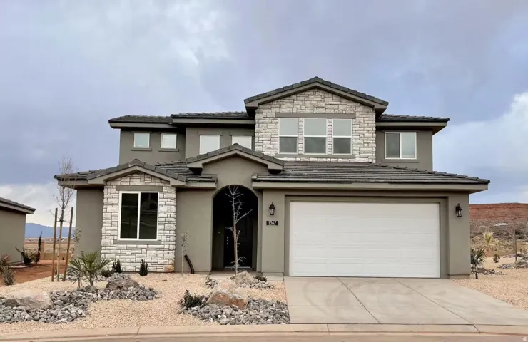 Modern stucco exterior with stone accents, a two-car garage, dark tile roofing, and desert landscaping