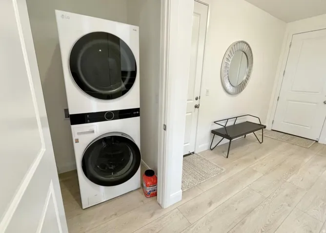 Dedicated laundry area featuring a stacked washer and dryer, light wood-finish flooring, and white paneled doors