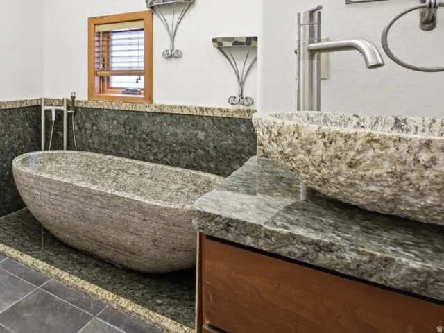 Bathroom featuring a stone soaking tub, stone vessel sink, and granite countertops