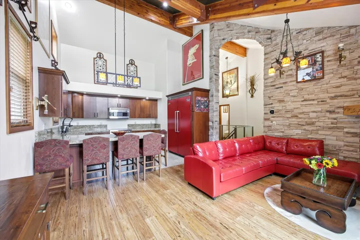 Open-concept living space featuring wood-finish flooring, exposed wood beams, and a stone accent wall
