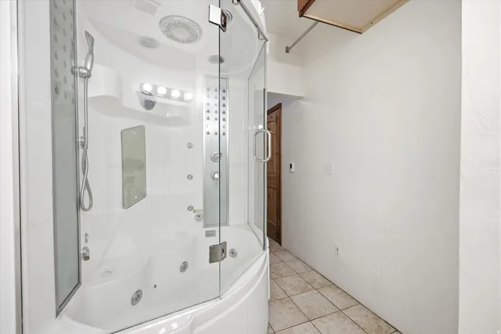 Enclosed shower and jetted tub combination featuring clear glass panels, a handheld showerhead, multiple body jets, and integrated lighting