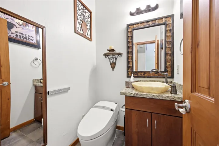 Bathroom featuring a vessel sink, wood-finish vanity with stone countertop, and a wall-mounted mirror.