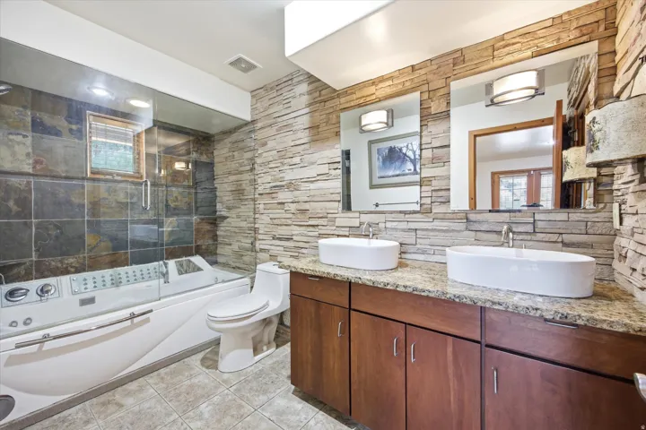 Bathroom featuring a jetted tub behind a glass enclosure,  and a dual vanity with vessel sinks