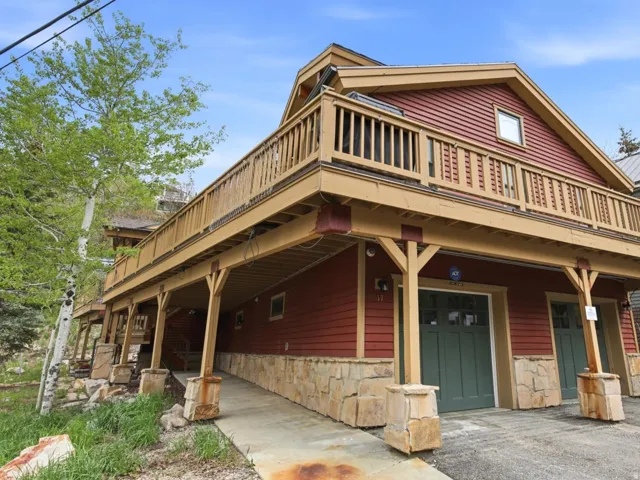 Multi-level property featuring red siding, stone accents, and a prominent second-story balcony with wood railings