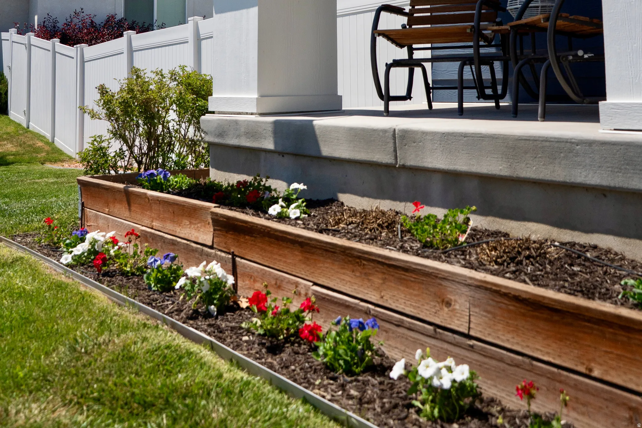 Tiered wood-finish raised garden beds with mature plantings, bordered by a manicured lawn