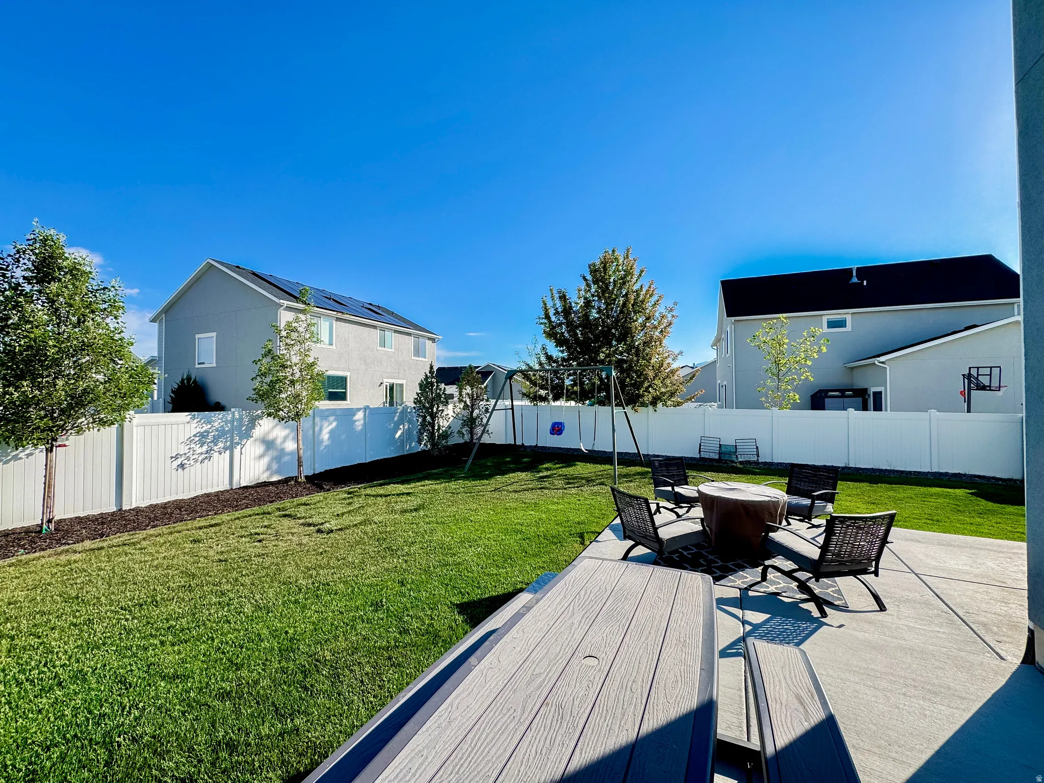 Expansive backyard featuring a lush lawn, concrete patio, and white privacy fencing