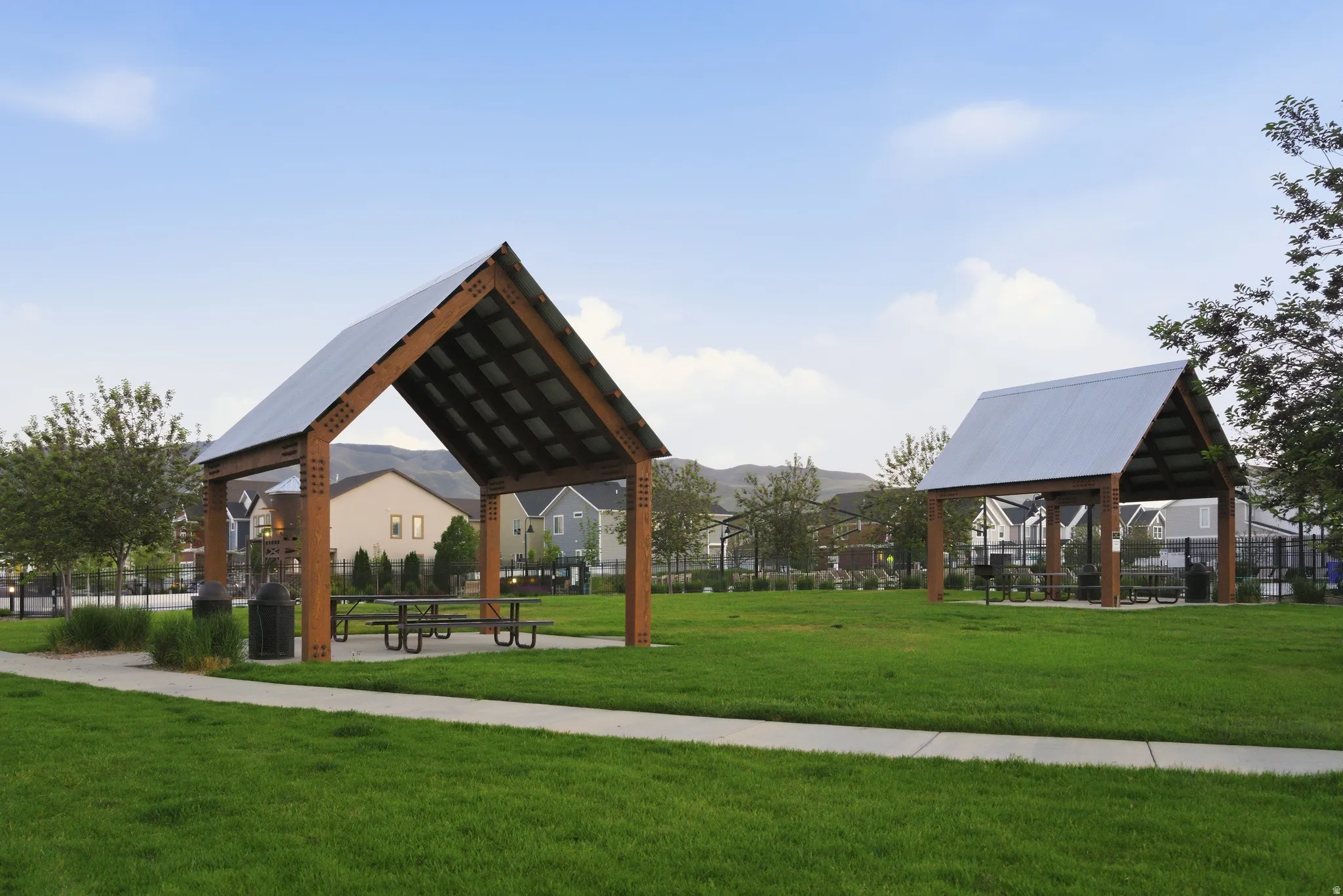 Expansive green space featuring multiple covered picnic areas with metal roofs and wooden beam construction