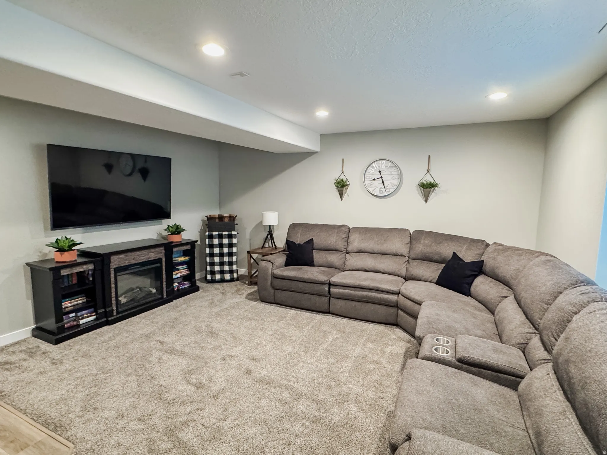 Carpeted recreation room featuring an entertainment console with an integrated electric fireplace, built-in shelving, and recessed ceiling lighting