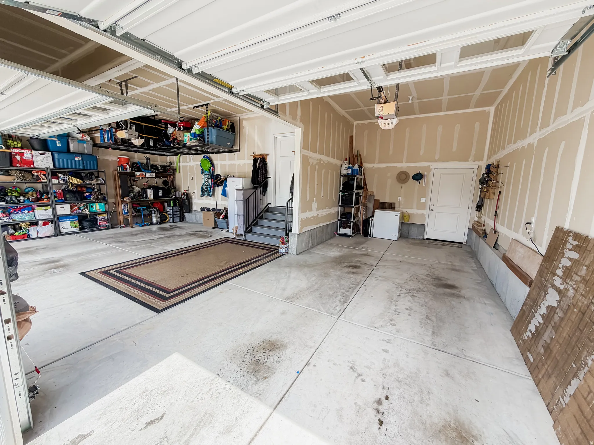 Spacious garage featuring concrete flooring, an overhead garage door, and interior access via a white door and staircase