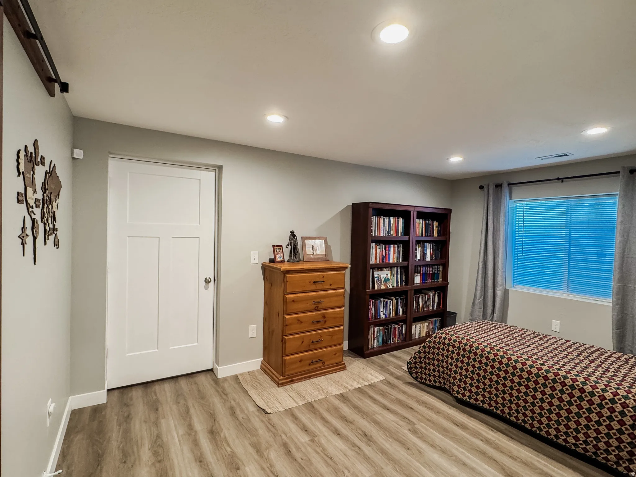 Spacious room featuring wood-finish flooring, recessed lighting, a modern three-panel door, and a window with blinds and drapes