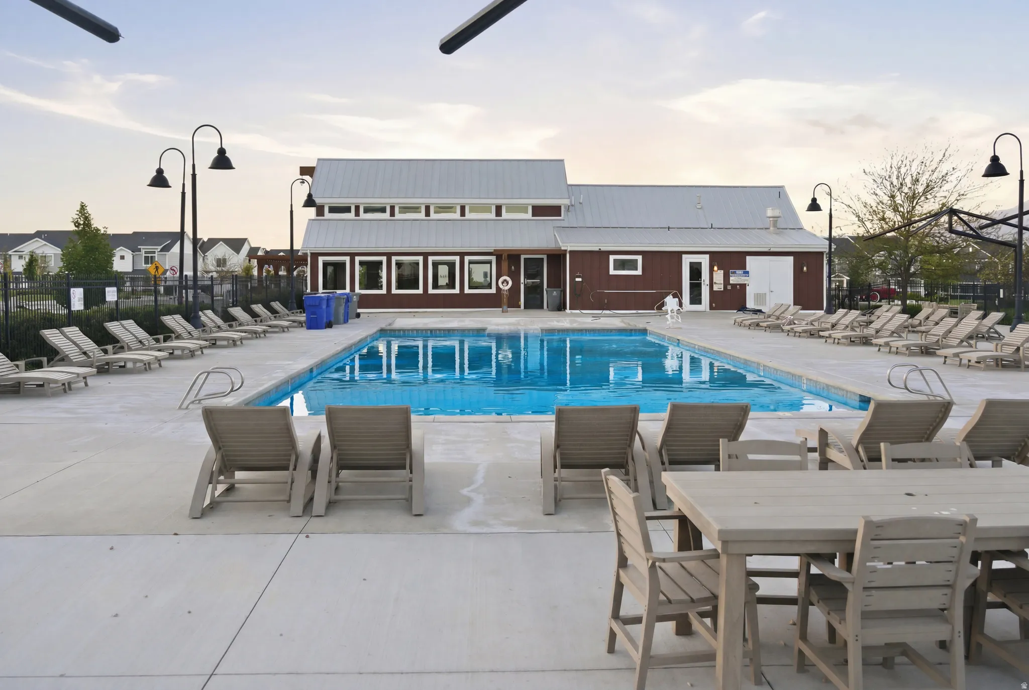 Expansive outdoor pool area featuring a rectangular swimming pool with integrated steps, a surrounding concrete deck, and a clubhouse structure with a metal roof