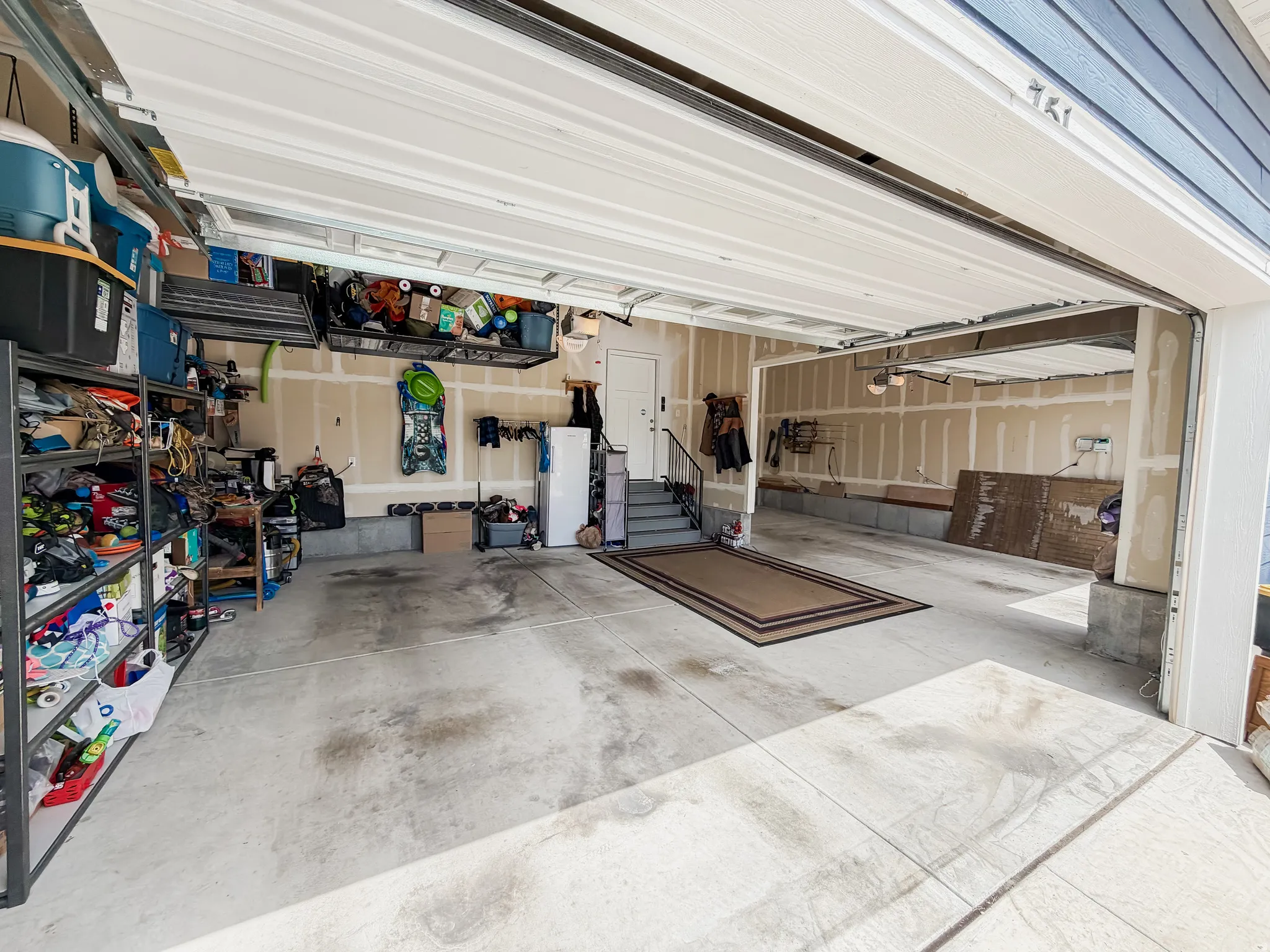 Two-car garage featuring a concrete floor, overhead door, and interior access door with stairs