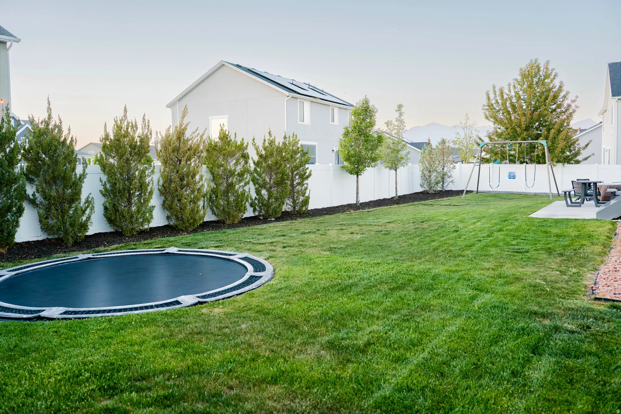 Expansive backyard featuring a large lawn area, mature perimeter trees, and a white privacy fence