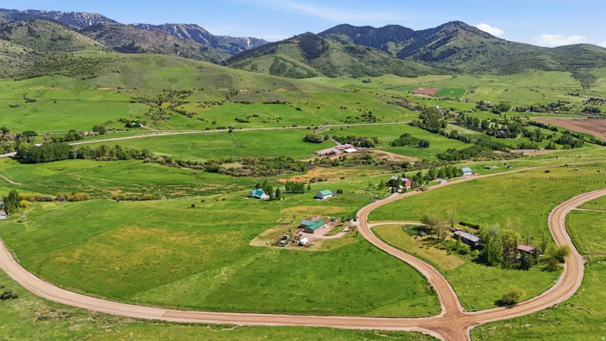 Expansive green landscape with mountain backdrop, featuring winding unpaved roads, scattered structures, and natural waterways