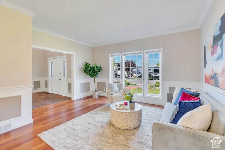 Expansive living area featuring wood-finish flooring, a wall of three large windows, crown molding, and wainscoting