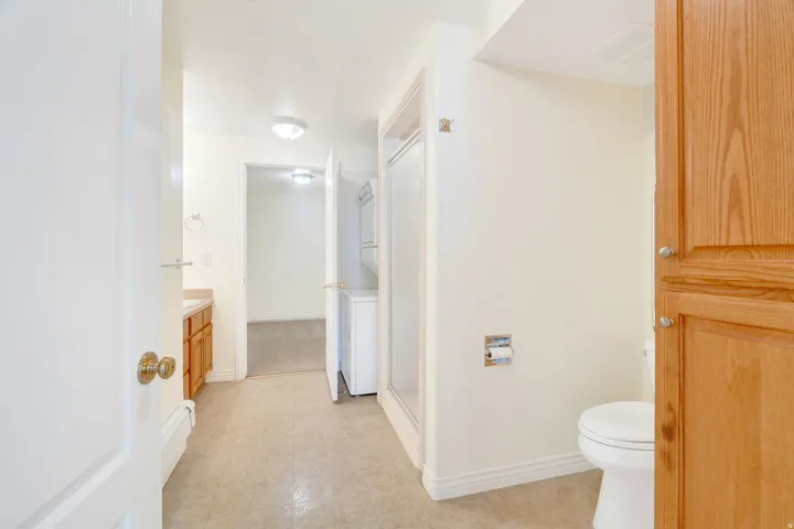 Bathroom featuring neutral tile flooring, a built-in wood vanity with a countertop and sink, a toilet, and a glass-enclosed shower