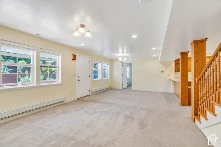 Expansive carpeted room featuring multiple windows, a white entry door, and a built-in wet bar with wood cabinetry