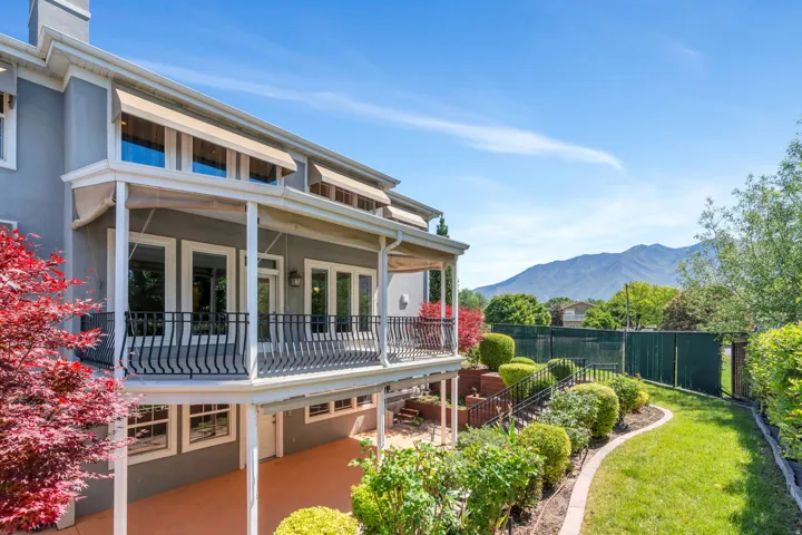 Multi-level exterior featuring a covered balcony with wrought iron railing, upper-level retractable awnings, and a lower-level patio