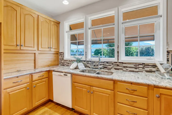 Kitchen featuring wood-finish cabinetry, light-toned stone countertops, and a mosaic tile backsplash