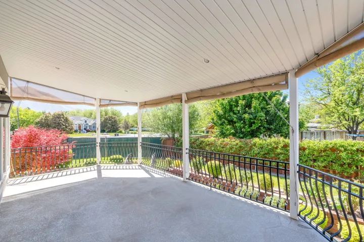 Spacious covered patio with concrete flooring, white paneled ceiling, and intricate wrought iron railing