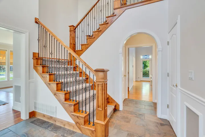 Grand staircase featuring natural wood newel posts, handrails, and treads with black wrought iron balusters and carpeted runners