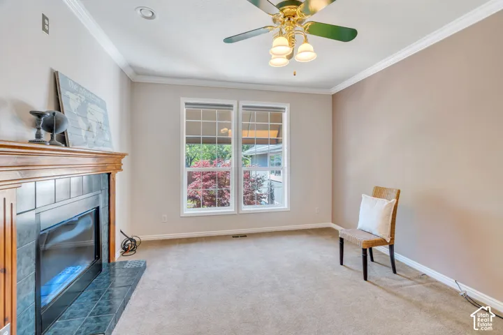 Room featuring a fireplace with a wood mantle and dark tile surround, two windows, carpeted flooring, and crown molding