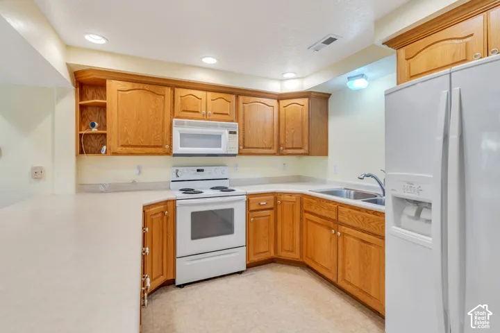 Kitchen featuring wood cabinetry, white appliances, recessed lighting, and a double basin stainless steel sink