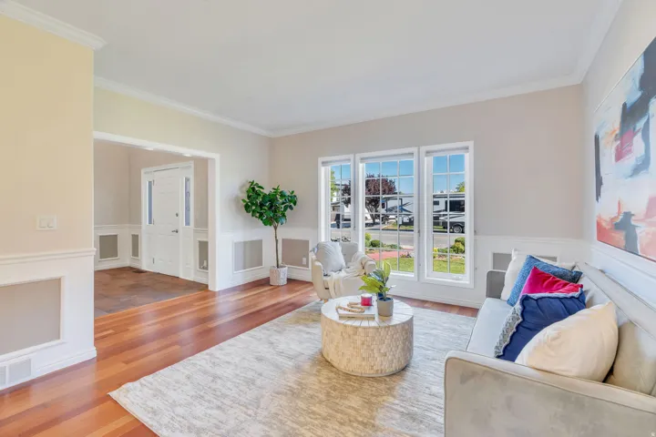 Expansive living area featuring wood-finish flooring, a wall of three large windows, crown molding, and wainscoting