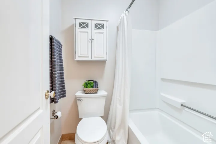 Bathroom featuring a white toilet, wall-mounted storage cabinet with X-detail doors, and a white bathtub with a shower surround