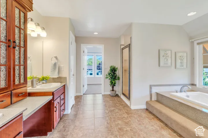 Spacious bathroom featuring dual wood-finish vanities with integrated sinks, a tiled shower enclosure, a built-in soaking tub with steps, and neutral floor tiling