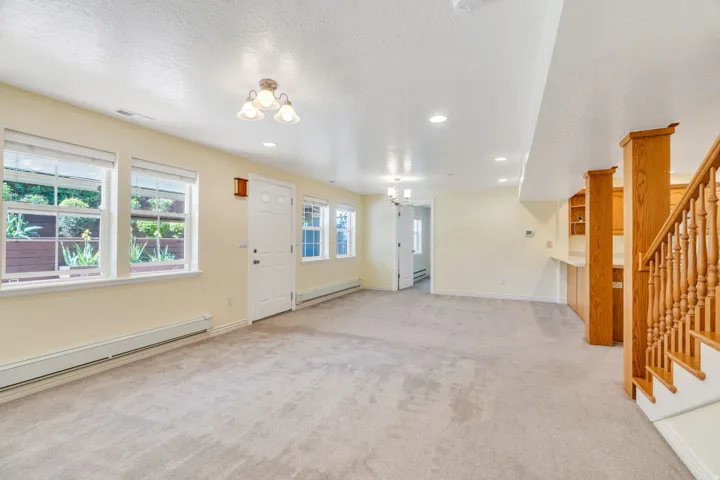 Expansive carpeted room featuring multiple windows, a white entry door, and a built-in wet bar with wood cabinetry