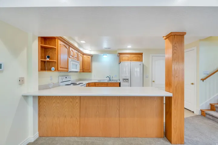 Kitchenette featuring wood cabinetry, white appliances, and a pass-through countertop