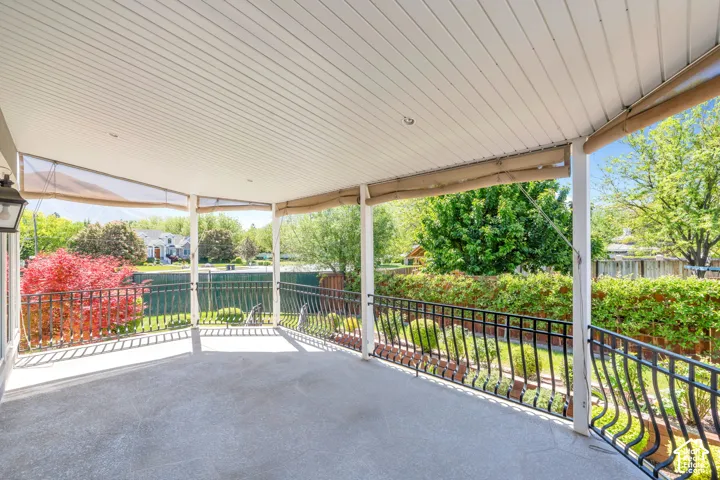 Spacious covered patio with concrete flooring, white paneled ceiling, and intricate wrought iron railing