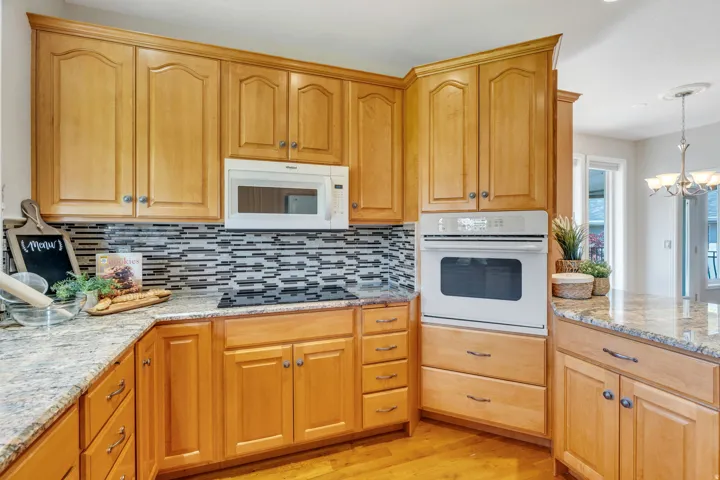 Kitchen with light wood cabinetry, granite countertops, a built-in oven, and a mosaic tile backsplash